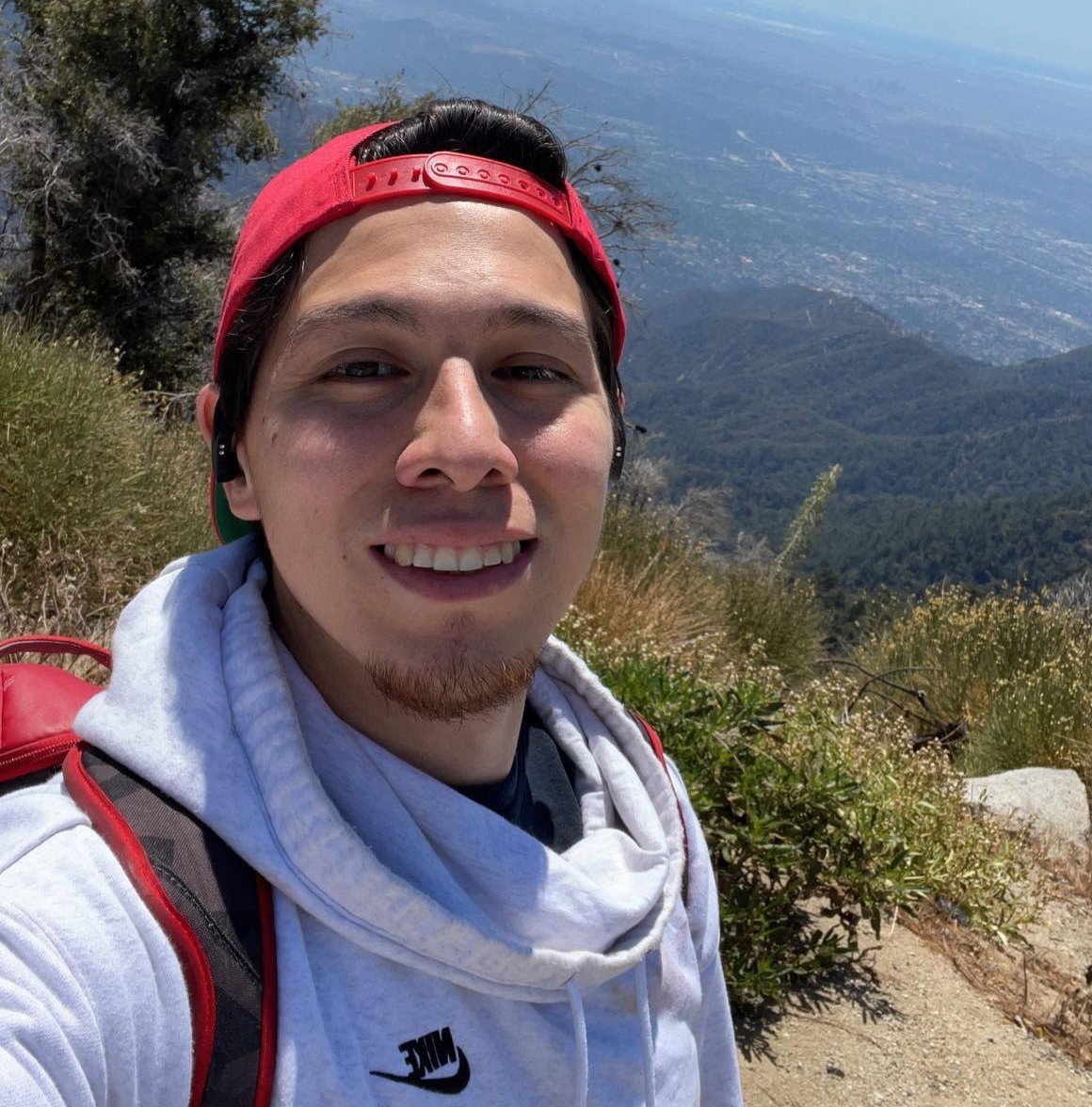 Selfie of me in a red hat and white hoodie hiking